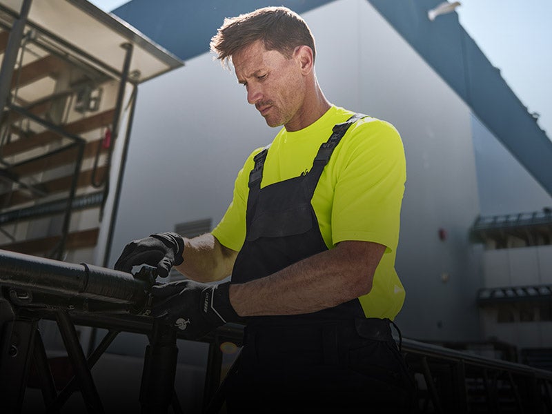 Handwerker trägt Latzhose und Neon-Shirt.