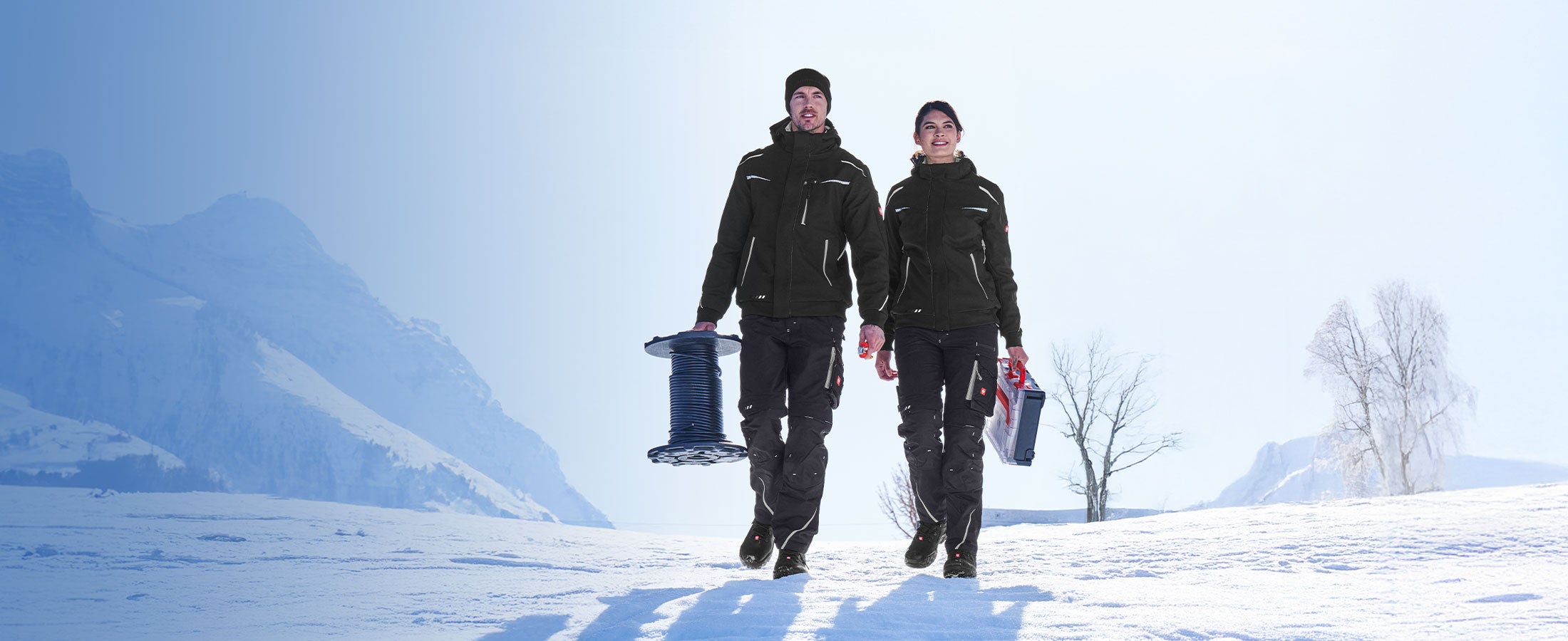 Een man en een vrouw lopen volledig gekleed in e.s.motion 2020 door een sneeuwlandschap.