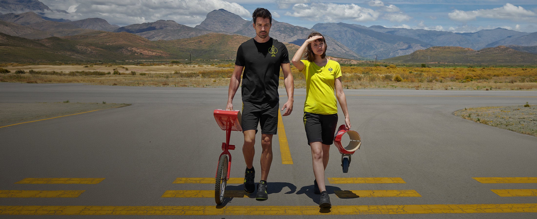 Deux personnes portant la collection e.s.trail marchent sur une piste devant un paysage montagneux.