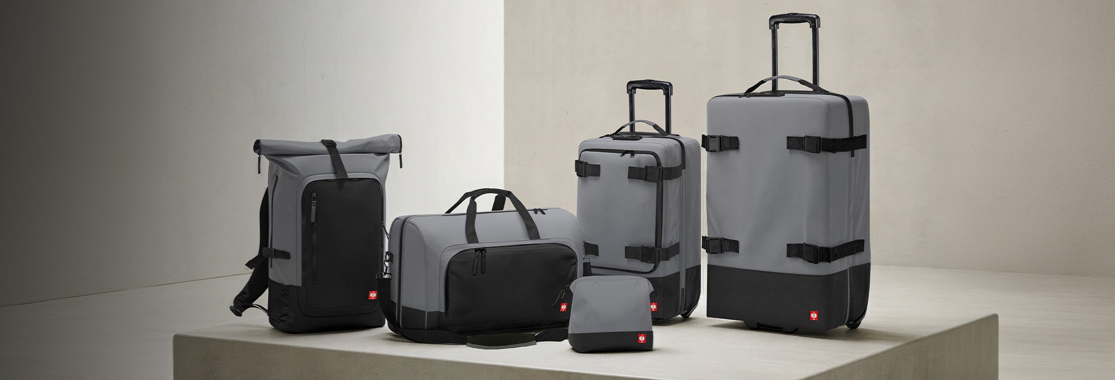 Grauer Rucksack, Reisetasche, Kulturbeutel und zwei Rollkoffer stehen auf einem Podest.