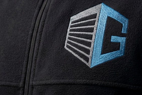 KI-generiert / modifiziert - Schwarze Jacke mit Reißverschluss und blau-grauem gesticktem Logo auf Brusthöhe.