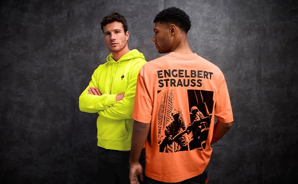 Un homme vêtu d'un pull à capuche vintage orange néon et un homme vu de dos vêtu d'un t-shirt vintage jaune néon. Au dos, on peut voir un imprimé sympa avec l'inscription engelbert strauss.