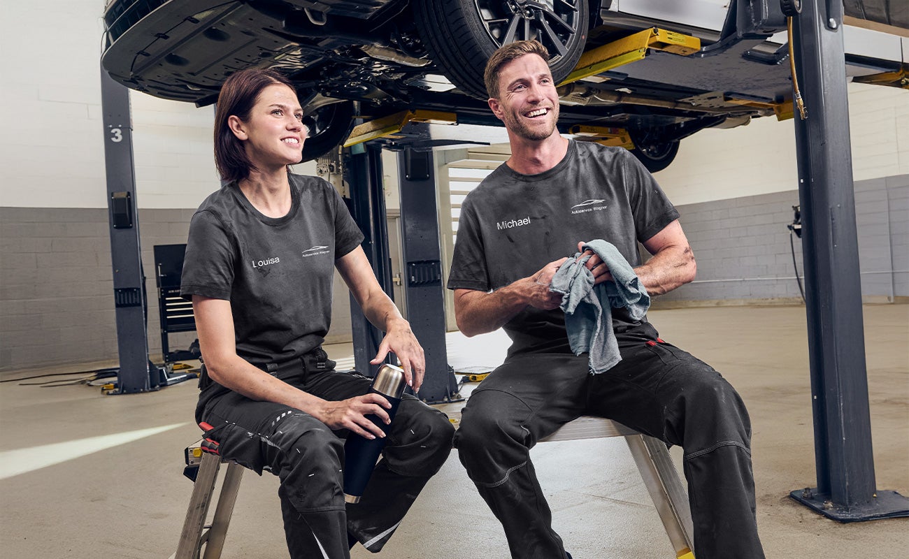 A woman and a man working in a car repair shop and wearing e.s.industry shirts