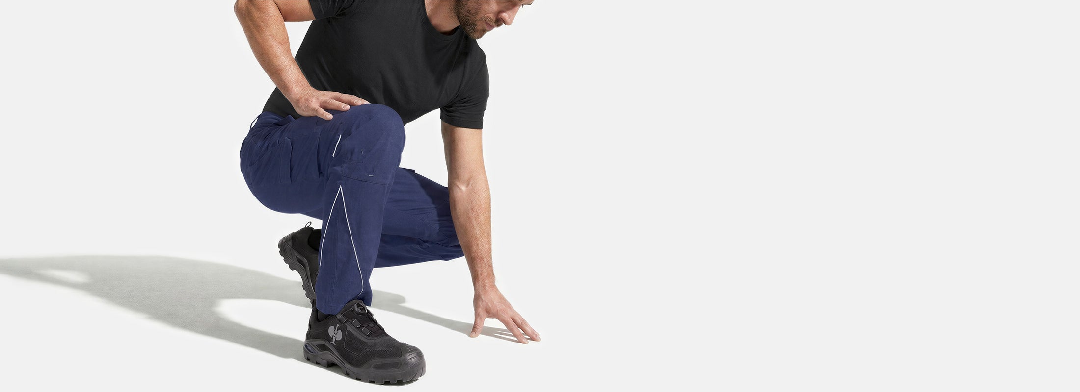 AI-generated / modified - Crouching person in blue work trousers and black work shoes on a light grey background.