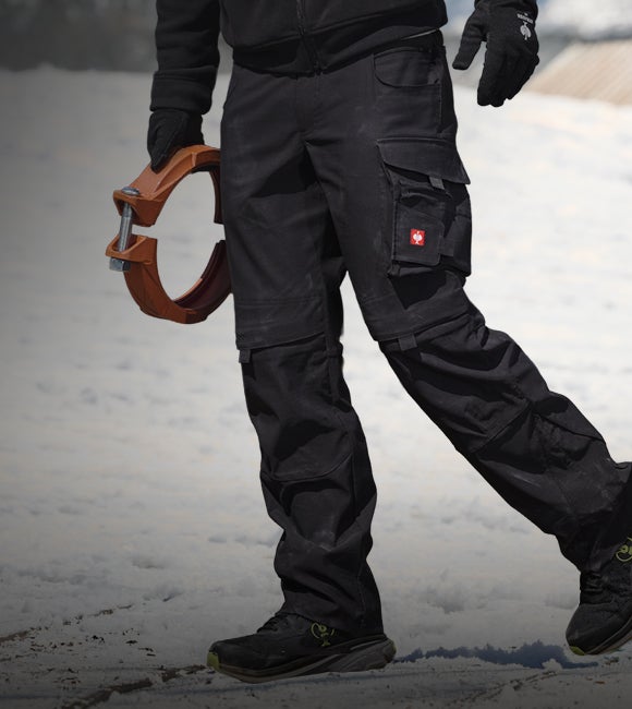 Man in grey workwear carrying a coiled hose in front of a helicopter.