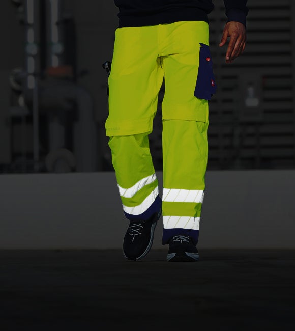Person in black work trousers, gloves and safety shoes carries a large clamp in the snow.