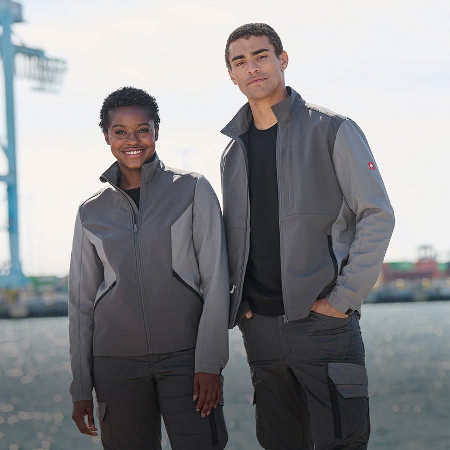 La femme et l’homme portent une veste Softshell e.s.trail pure en gris carbone / gris basalte
