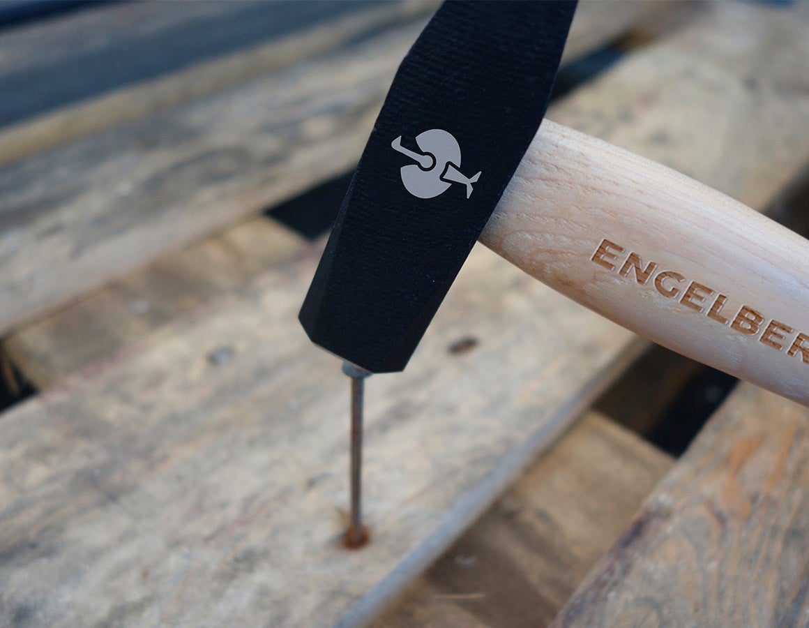 e.s. Schlosserhammer classic beim Einschlagen eines Nagels in eine Holzoberfläche, mit schwarzem Hammerkopf, Engelbert-Strauss-Prägung am Griff und weißem Logo