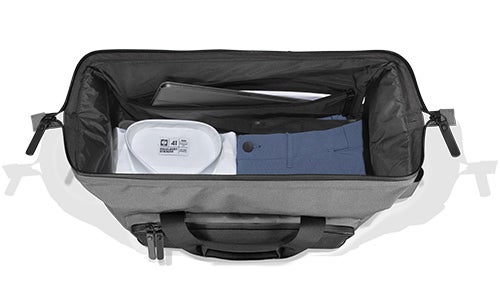 Grau-schwarze Reisetasche mit geöffneten Reißverschlüssen, im Inneren sind eine weiße Kulturtasche und ein blaues zusammengefaltetes Kleidungsstück sichtbar.