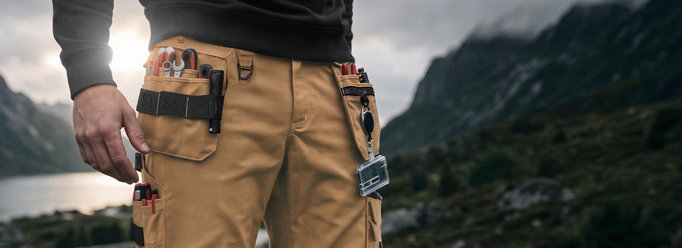 KI-generiert / modifiziert - Unterkörper einer Person in der Holster Bundhose e.s.line.nordic canvas mit Werkzeugen in den Taschen vor Berglandschaft.