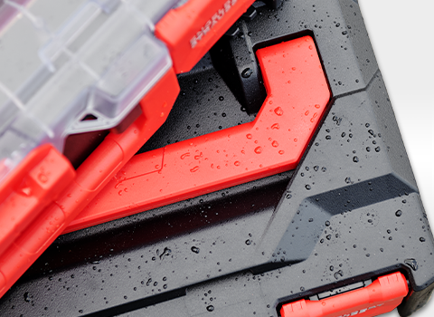 Close-up of a black STRAUSSbox with red latches and water droplets on the surface, indicating splash protection