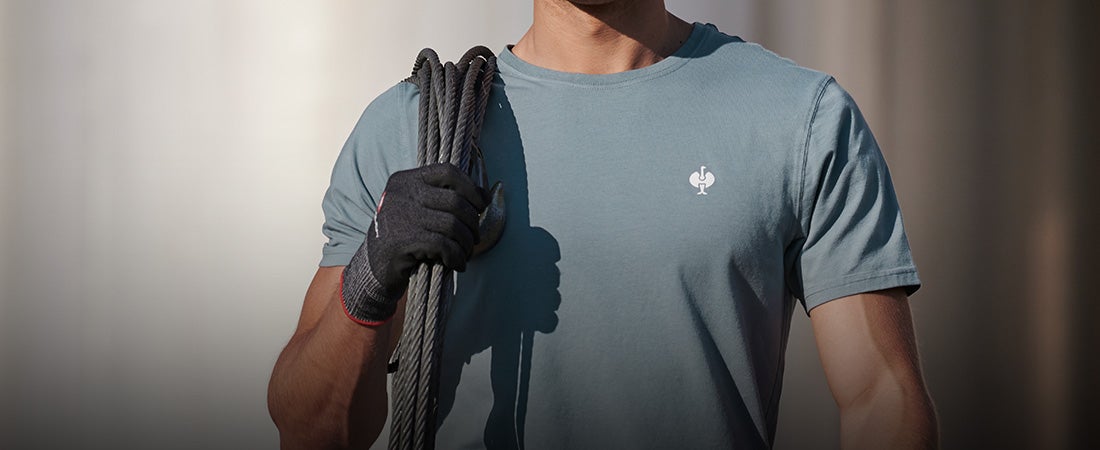 Person in a blue T-shirt with a glove holds a coiled rope over the shoulder.
