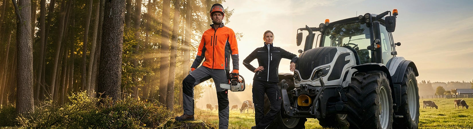 Man i orange-svart e.s. vision skogsjacka och e.s. skogsskyddsbyxor staplar ved medan en kvinna i svart/platinafärgad motion 2020 arbetsklädsel matar kor vid beteshagen.