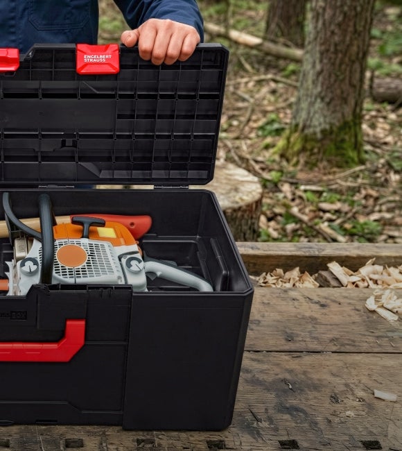 Open black toolbox with an axe on a wooden bench outdoors.