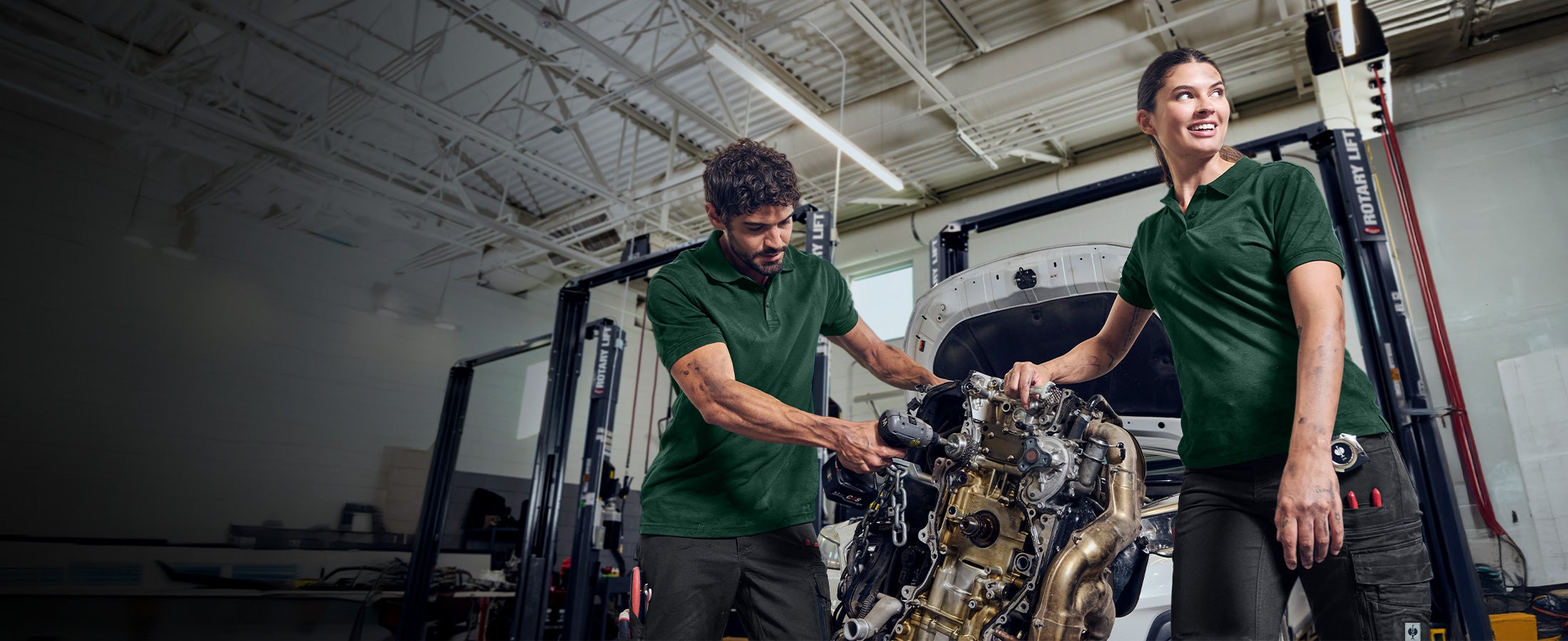 A woman and a man working in a car repair shop and wearing e.s.industry shirts