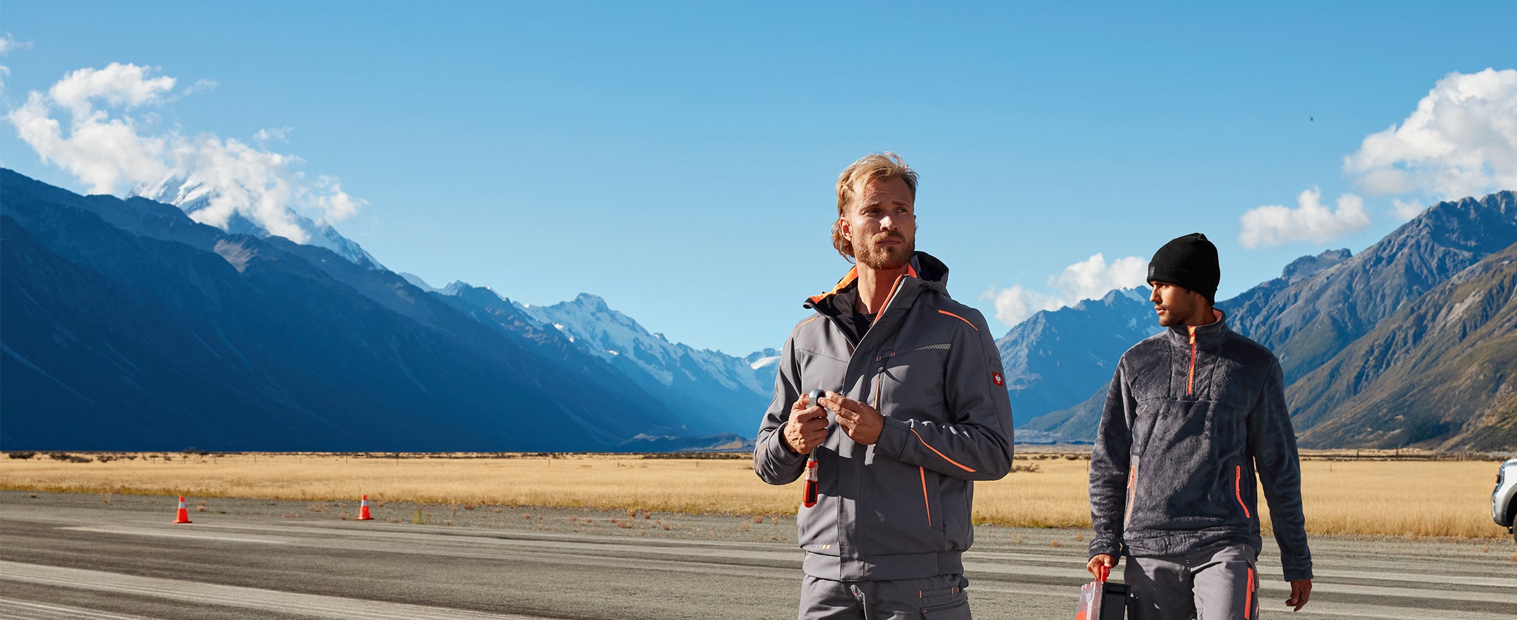 Two men wear the new e.s.motion2020 pieces in anthracite/hi-vis orange