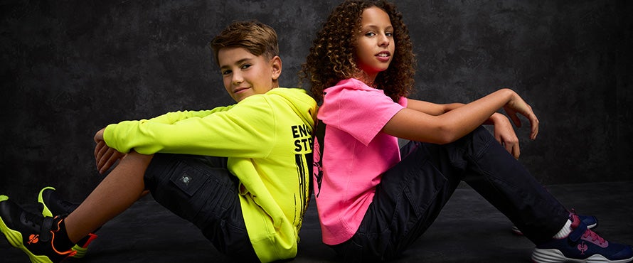 Two children sitting back to back wearing a neon yellow vintage hoody and a neon pink vintage shirt.